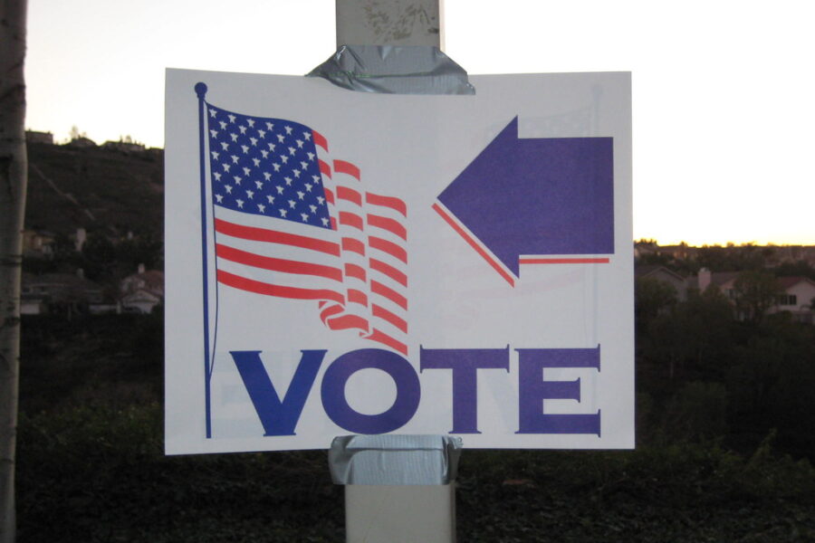 This image is of a sign that reads, "Vote" with an arrow pointing to an American Flag